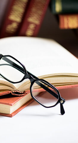 Stack of books with black men's glasses placed on the open book in library or on the white table