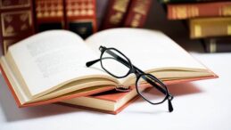 Stack of books with black men's glasses placed on the open book in library or on the white table